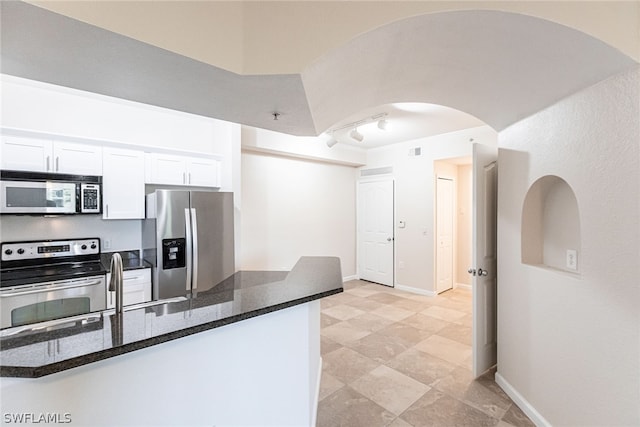 kitchen with appliances with stainless steel finishes, light tile floors, white cabinetry, rail lighting, and dark stone countertops