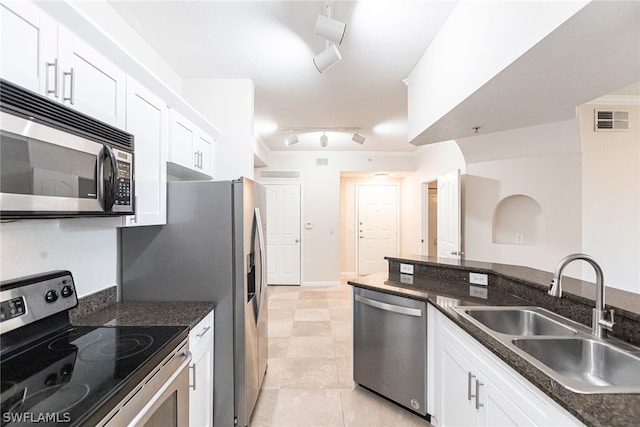 kitchen featuring white cabinets, sink, stainless steel appliances, dark stone countertops, and track lighting