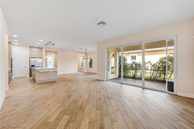 unfurnished living room featuring a healthy amount of sunlight, light wood-type flooring, and a chandelier