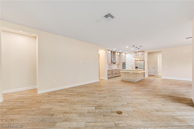 unfurnished living room featuring sink and light hardwood / wood-style floors