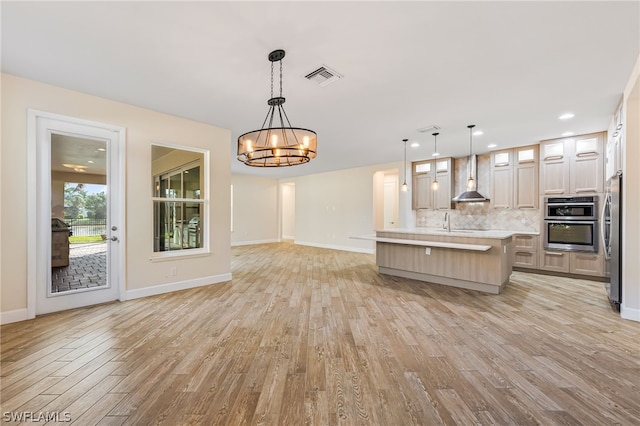 kitchen featuring light hardwood / wood-style flooring, wall chimney range hood, pendant lighting, and a kitchen island