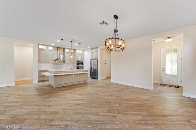 kitchen with stainless steel appliances, a center island with sink, tasteful backsplash, wall chimney exhaust hood, and pendant lighting