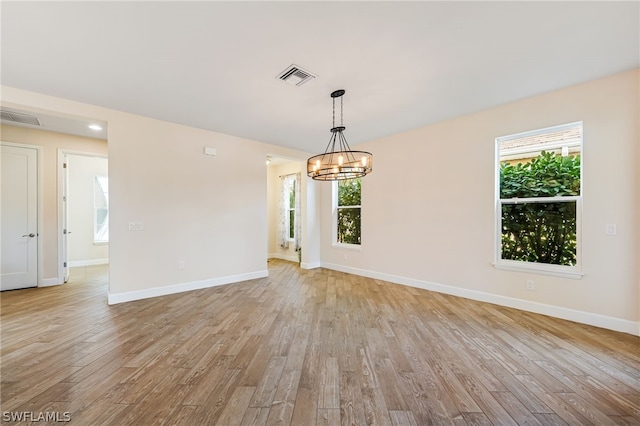 spare room with plenty of natural light, light hardwood / wood-style floors, and a chandelier