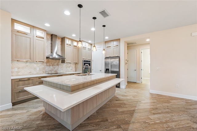 kitchen featuring backsplash, appliances with stainless steel finishes, wall chimney exhaust hood, a kitchen island with sink, and hardwood / wood-style floors