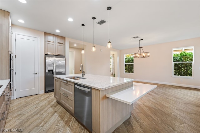 kitchen featuring hanging light fixtures, light wood-type flooring, stainless steel appliances, sink, and an island with sink