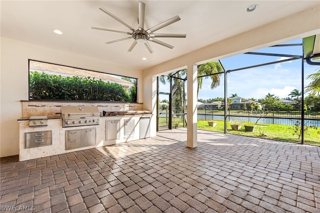 view of terrace with glass enclosure, a water view, ceiling fan, area for grilling, and exterior kitchen