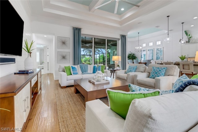 living room featuring a raised ceiling, plenty of natural light, light hardwood / wood-style floors, and ceiling fan with notable chandelier