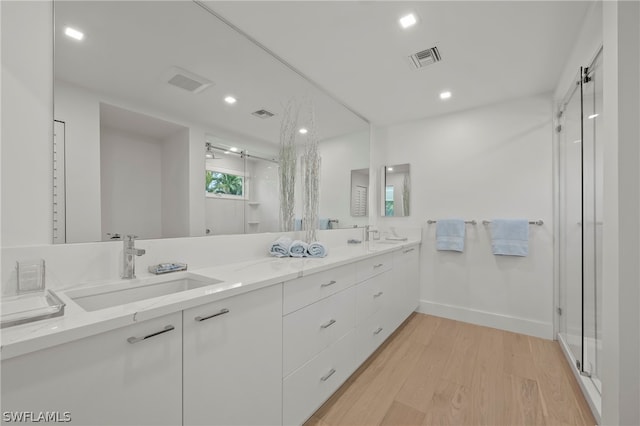 bathroom featuring hardwood / wood-style flooring, a shower with door, and double vanity