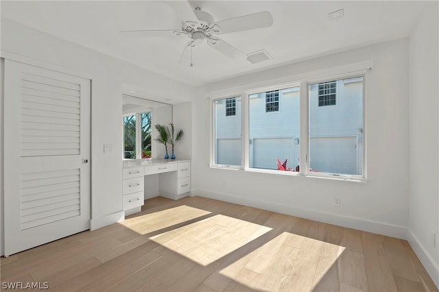 unfurnished bedroom with a closet, light hardwood / wood-style flooring, built in desk, and ceiling fan