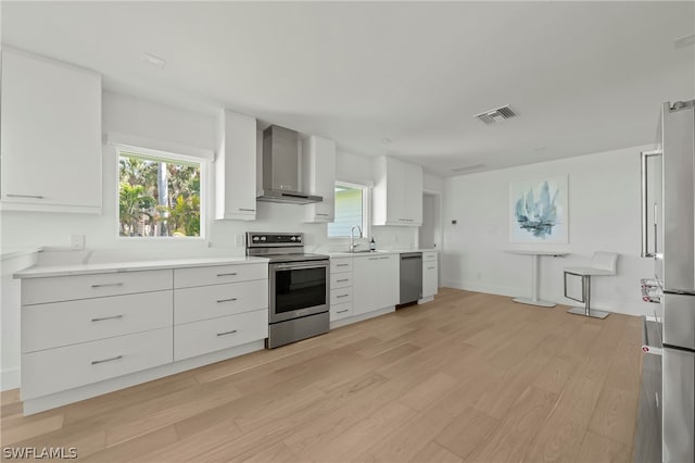 kitchen featuring stainless steel appliances, light hardwood / wood-style floors, wall chimney exhaust hood, white cabinets, and sink