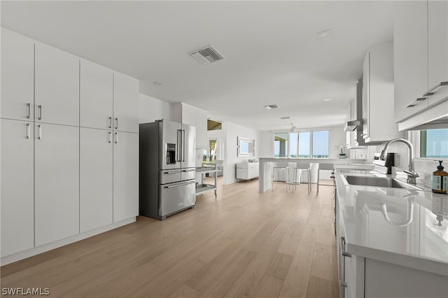 kitchen with high end fridge, white cabinets, sink, and light wood-type flooring