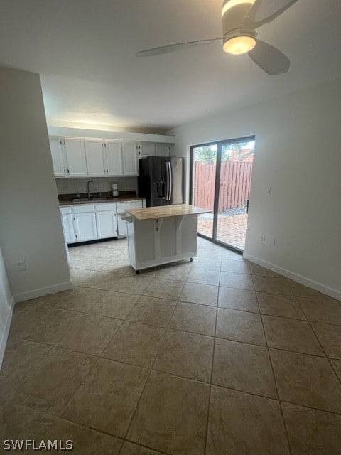 kitchen with a kitchen island, ceiling fan, black refrigerator with ice dispenser, white cabinetry, and light tile floors