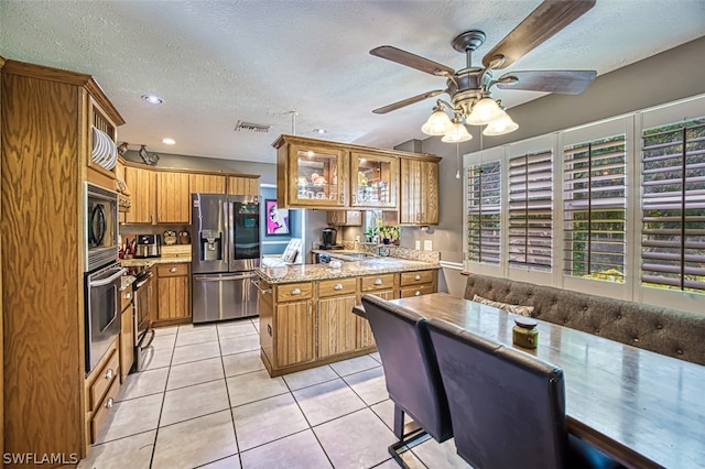 kitchen with light tile patterned floors, ceiling fan, stainless steel appliances, light stone countertops, and a textured ceiling