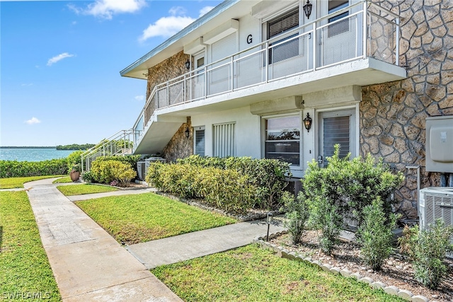 view of front facade featuring a water view, central air condition unit, a balcony, and a front yard