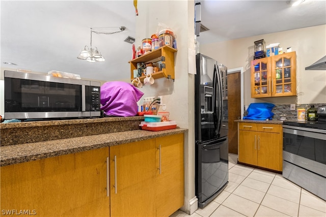 kitchen with appliances with stainless steel finishes, dark stone counters, light tile flooring, and decorative light fixtures