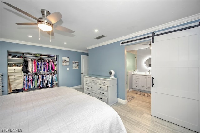 bedroom featuring crown molding, light wood-type flooring, a closet, ceiling fan, and a barn door