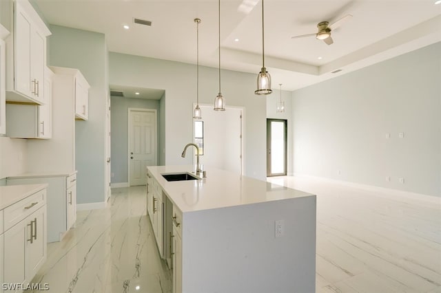 kitchen with white cabinets, a tray ceiling, sink, a center island with sink, and ceiling fan