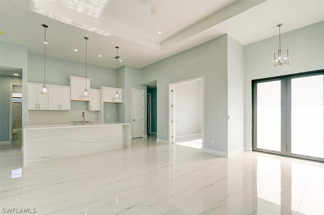 kitchen featuring white cabinets, light tile flooring, decorative light fixtures, a high ceiling, and a kitchen island with sink