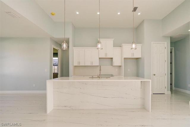 kitchen featuring hanging light fixtures, a high ceiling, a kitchen island with sink, white cabinetry, and sink