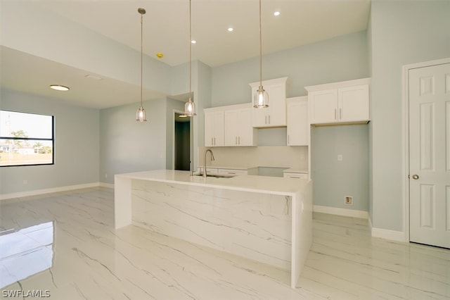 kitchen with pendant lighting, white cabinets, sink, and an island with sink