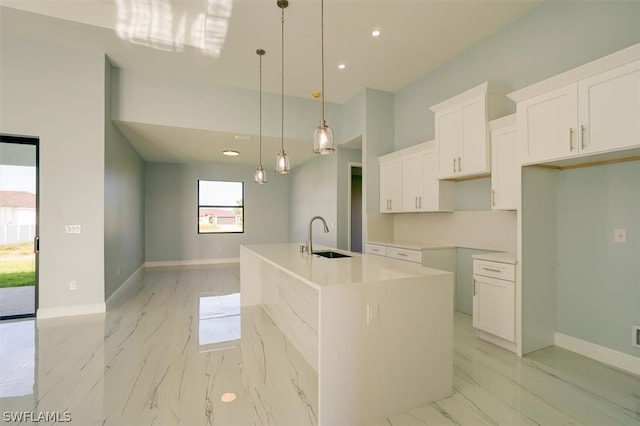 kitchen featuring white cabinets, sink, a center island with sink, and decorative light fixtures