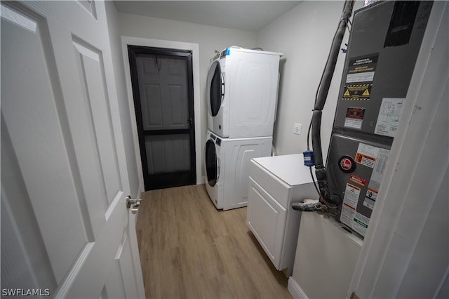 laundry room featuring cabinets, light hardwood / wood-style flooring, and stacked washer and clothes dryer