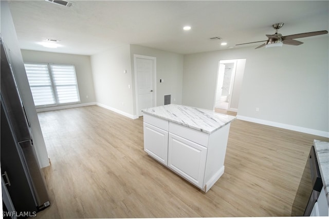 kitchen featuring light stone counters, light hardwood / wood-style floors, white cabinetry, a kitchen island, and ceiling fan