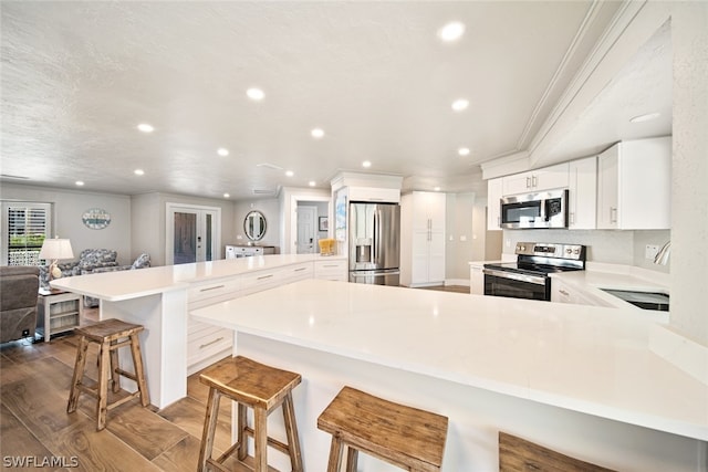 kitchen featuring a kitchen breakfast bar, wood-type flooring, white cabinets, stainless steel appliances, and a kitchen island