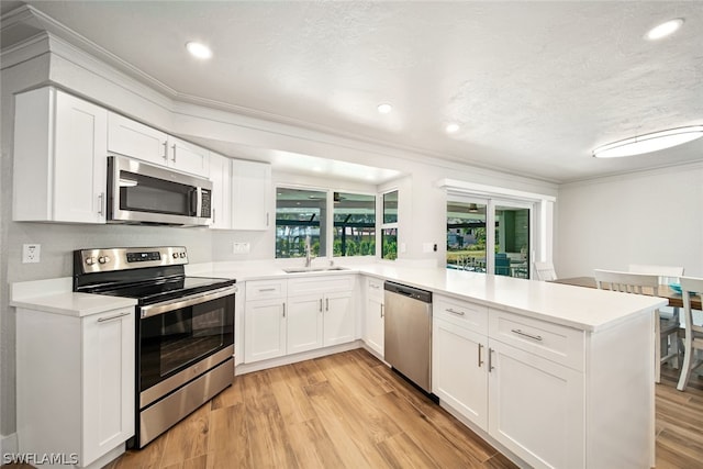 kitchen with light hardwood / wood-style floors, appliances with stainless steel finishes, kitchen peninsula, and white cabinetry