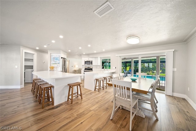 dining room featuring ornamental molding, sink, light wood-type flooring, and a textured ceiling