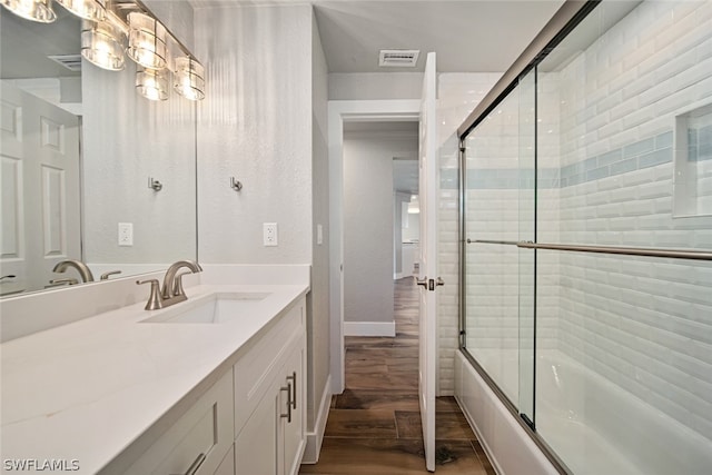 bathroom with hardwood / wood-style flooring, enclosed tub / shower combo, and vanity