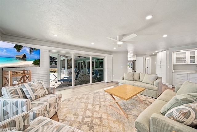 living room featuring light hardwood / wood-style flooring, ceiling fan, a textured ceiling, and ornamental molding