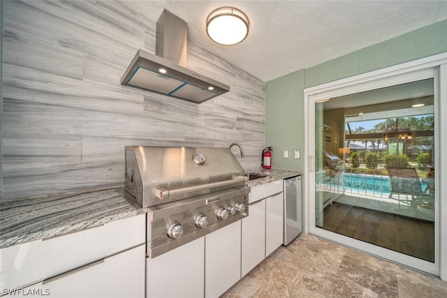 kitchen featuring light stone countertops, wall chimney range hood, white cabinetry, light tile floors, and stainless steel dishwasher