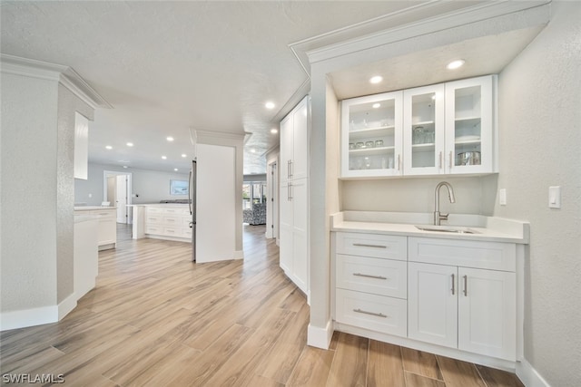 bar featuring white cabinets, sink, light wood-type flooring, and a textured ceiling