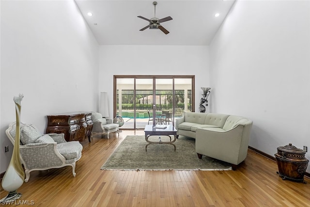 living room with a high ceiling, ceiling fan, and light hardwood / wood-style flooring