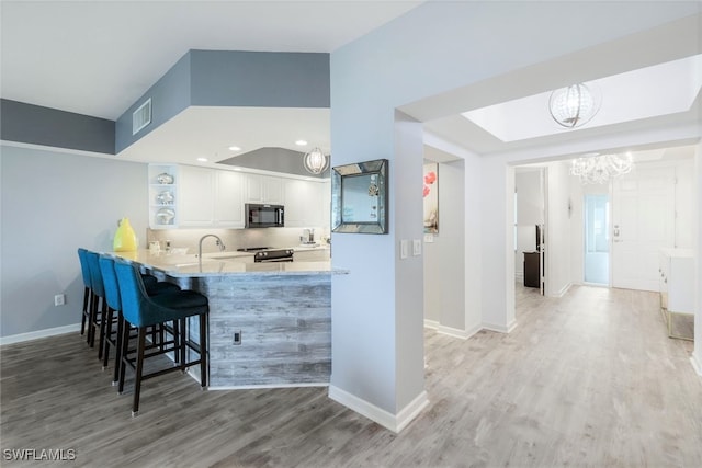 kitchen featuring a breakfast bar area, kitchen peninsula, black appliances, light wood-type flooring, and white cabinets