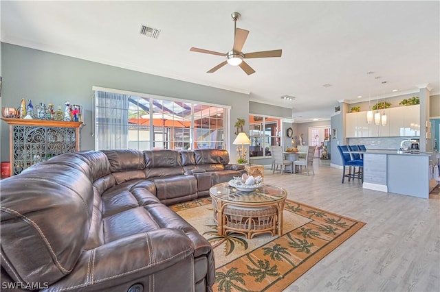 living room featuring ornamental molding, light wood-type flooring, visible vents, and a ceiling fan