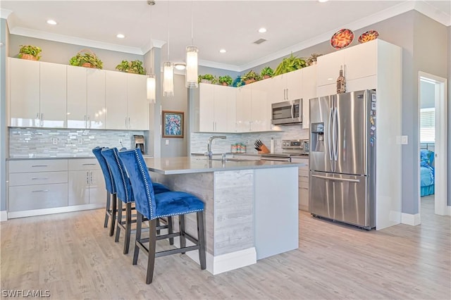 kitchen with a breakfast bar area, stainless steel appliances, hanging light fixtures, ornamental molding, and a sink