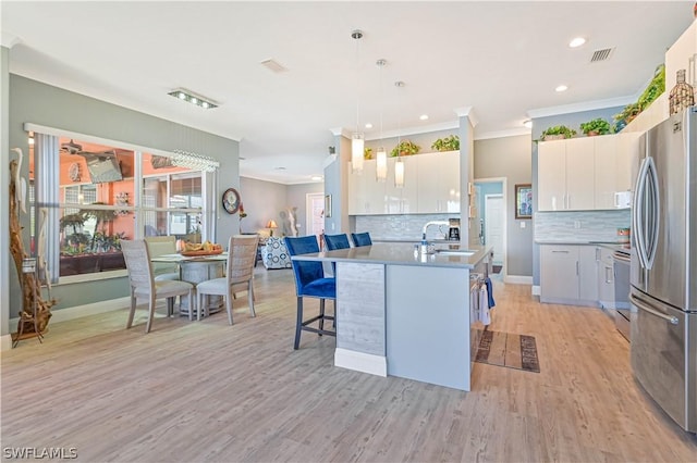 kitchen featuring pendant lighting, visible vents, light wood-style floors, freestanding refrigerator, and a sink