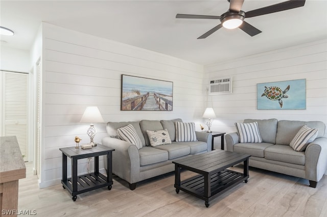 living room with a wall unit AC, wood walls, light hardwood / wood-style floors, and ceiling fan