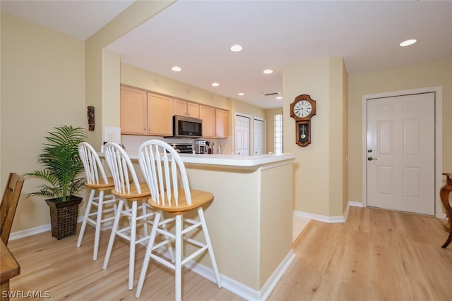 kitchen with light brown cabinets, kitchen peninsula, light wood-type flooring, and a breakfast bar