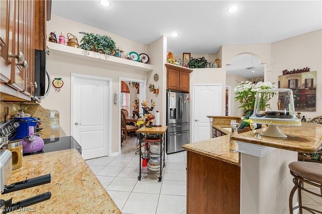 kitchen featuring appliances with stainless steel finishes, a kitchen bar, light tile flooring, backsplash, and light stone countertops