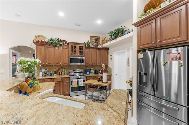 kitchen featuring appliances with stainless steel finishes, sink, backsplash, and light stone counters