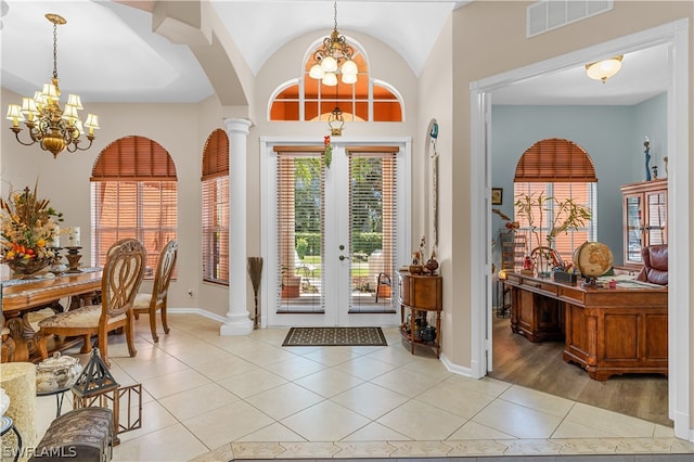 tiled foyer featuring a chandelier, a towering ceiling, french doors, and decorative columns