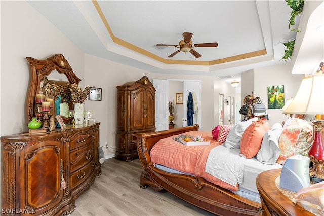 bedroom with light hardwood / wood-style flooring, ceiling fan, and a tray ceiling