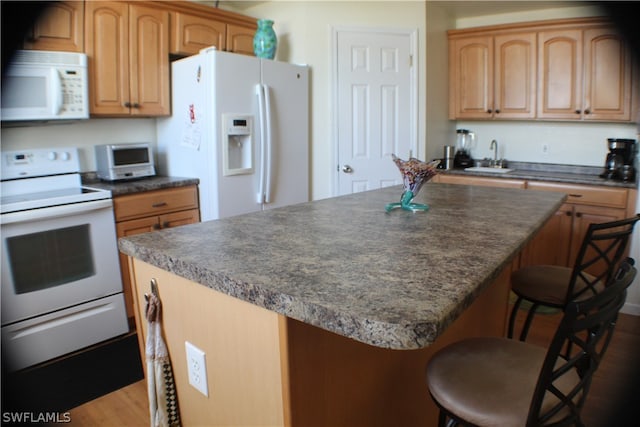 kitchen with a breakfast bar area, white appliances, hardwood / wood-style flooring, sink, and a center island