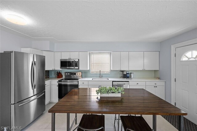 kitchen with white cabinets, appliances with stainless steel finishes, sink, and light tile flooring