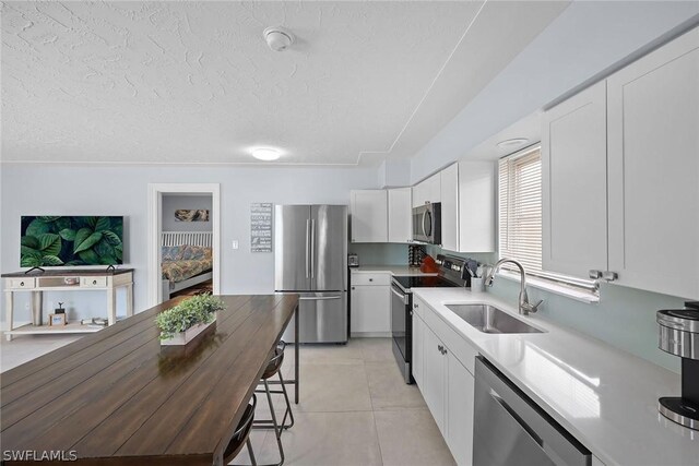 kitchen featuring stainless steel appliances, light tile floors, white cabinetry, sink, and a textured ceiling