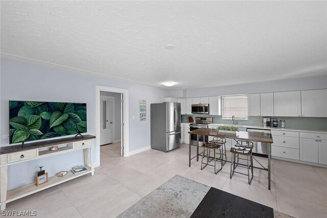 kitchen with white cabinetry, a textured ceiling, stainless steel appliances, sink, and light tile floors