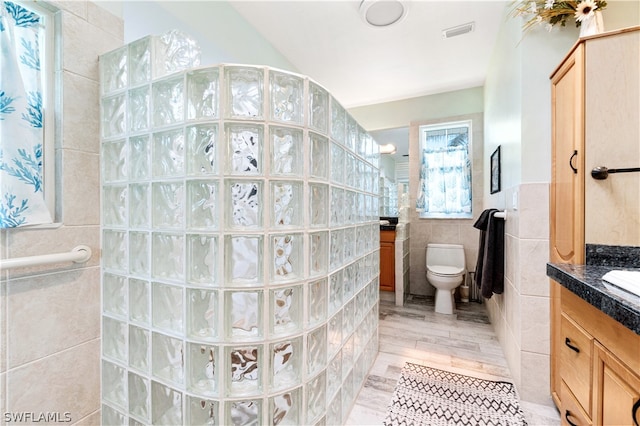 bathroom featuring tile floors, vanity, toilet, and tile walls